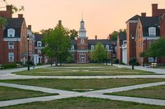 the sun is setting in front of several brick buildings with grass and trees on each side