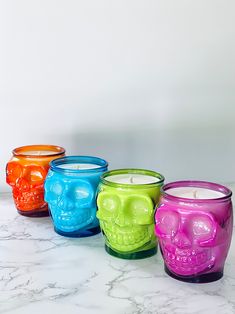 four colorful candles with skulls on them sitting next to each other in front of a white wall