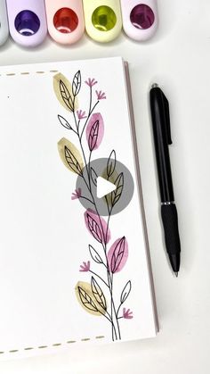 an open notebook with markers and paint next to it on a white surface, surrounded by four different colors of ink