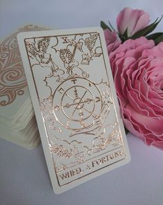 two white cards with gold foil on them next to pink roses and a rose bud