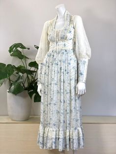 vintage lace trimmed blue & white floral print cotton voile prairie midi/maxi length dress full lace gigot sleeves w/ zippers at cuffs scoop neckline w/ lace & ribbon trimmed lace up corset bodice full gathered skirt w/ lace ruffle at hem & attached sash/tie 'Gunne Sax by Jessica San Francisco' 'Joseph Magnin' size tag 7, fits a modern x-small/small 32+ inch bust 26 inch waist 38 inch hip measurement at lining 12 1/2 inch shoulder measurement 3 1/2 inch cuff diameter 52 inch dress length 36 1/2 Feminine Fitted Prairie Dress With Long Sleeves, Fitted Vintage Dress With Lace Trim For Fall, Fitted Prairie Dress In Pastoral Style, Spring Fitted Midi Length Prairie Dress, Fitted Maxi Dress With Lace Patchwork For Daywear, Spring Maxi Dress With Lace Trim And Square Neck, Fitted Lace Patchwork Maxi Dress For Daywear, Spring Vintage Dress With Lace Trim And Fitted Bodice, Spring Vintage Dress With Fitted Bodice And Lace Trim