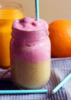 a smoothie in a mason jar next to two oranges