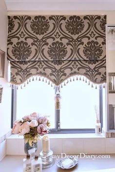 a bathroom window with an ornate valance and flowers in the vase on the counter