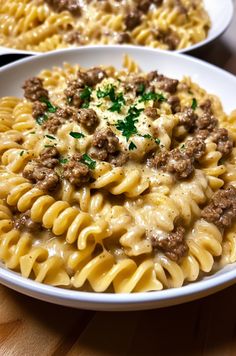 two white plates filled with pasta and meat on top of a wooden table in front of another plate