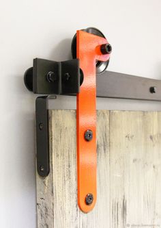 an orange and black handle on a wooden door with two hooks hanging from it's side