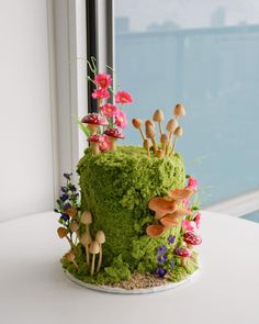 a green cake with mushrooms and flowers on it sitting on a table next to a window