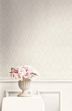 a vase filled with pink flowers sitting on top of a white table next to a wall