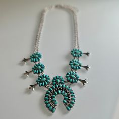 This statement piece is sure to make a statement at any event: the It Takes Two Squash Blossom Necklace. Features include a choice of turquoise or turquoise and white, a 22" silver chain with a 3" adjustable clasp, 7 mini stone conchos for added character, and a double chain with a 2" squash blossom. Feel fashionable and distinctive! Squash Blossom, It Takes Two, Squash Blossom Necklace, Double Chain, Statement Pieces, Silver Chain, Blossom, Take That, Turquoise