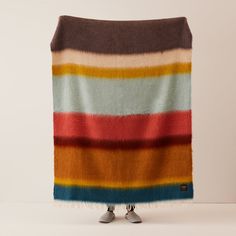 a multicolored striped blanket draped on top of a white surface with two legs standing in front of it