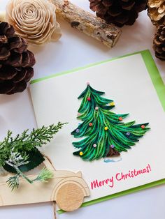 a card with a christmas tree on it next to pine cones and other holiday decorations