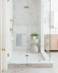 a bathroom with a glass shower door and white tile flooring, along with a potted plant in the corner