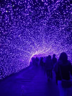 people walking through a tunnel covered in purple lights