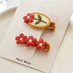 two crocheted hair clips with flowers on them sitting on top of a white plate