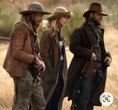 three people standing in the middle of a field wearing hats and trench coats, all looking at something