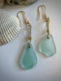 two sea glass drop earrings on a white table next to a shell and seashell