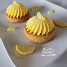 two small cakes with lemon icing on a white plate next to slices of lemon