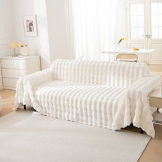 a white couch sitting in a living room on top of a hard wood floor next to a window