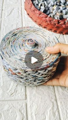 a hand holding a roll of paper next to a basket filled with rocks