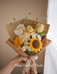 a person holding a bouquet of flowers in front of a window with the words flora crochet studio written on it