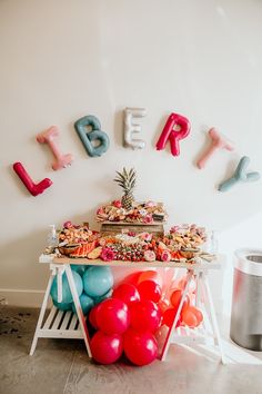 a table topped with lots of food and balloons next to a sign that says happy