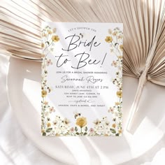 a white and yellow floral bridal party card on a plate next to palm leaves