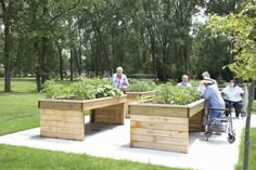 several people are sitting around in the park with raised planters on each side and one person pushing a wheelbarrow behind them