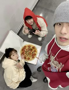 three people sitting at a table with pizza in front of them and one person holding a camera