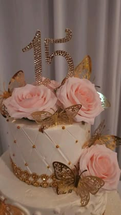 a white cake with pink roses and butterflies on top is surrounded by gold glitters