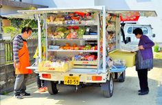 two people standing in front of a truck with food and drinks on the back,