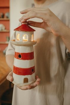 a woman is holding a lighthouse shaped candle holder