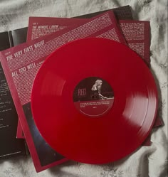 a red vinyl record sitting on top of a bed next to two booklets and an album