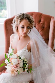 a bride sitting in a chair with her bouquet and veil over her head looking down