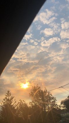 the sun is setting over some trees and houses in the distance, as seen from inside a car