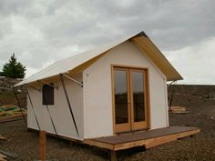 a small white building sitting on top of a dirt field next to a wooden platform