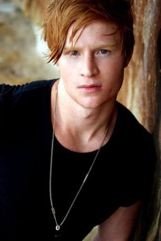 a young man with red hair leaning against a tree