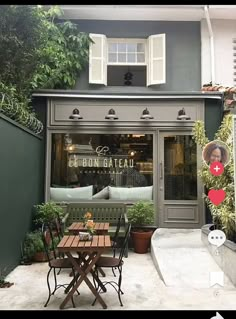 the outside of a restaurant with tables and chairs in front of it, surrounded by greenery