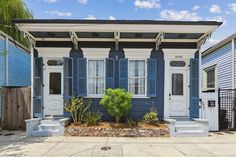 a blue and white house with shutters on the front door is next to a tree