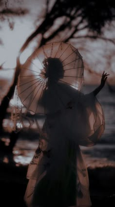 a woman holding an umbrella standing in front of the ocean at sunset with her arms outstretched