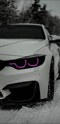 the front end of a white car with pink lights on it's headlights in the snow