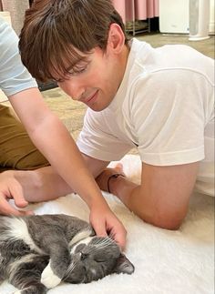 a man is petting a cat on the bed while another person looks at it