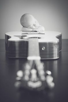 a black and white photo of a baby sleeping on top of a guitar with its head resting on it