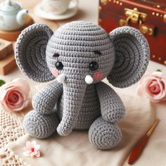 a crocheted gray elephant sitting on top of a table next to pink flowers