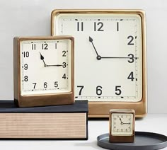 three different clocks sitting next to each other on top of a white table with books