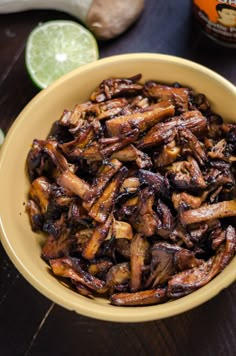 a yellow bowl filled with cooked mushrooms next to sliced limes and an onion wedge