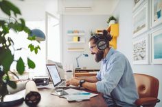 a man sitting at a desk with headphones on his ears working on a laptop