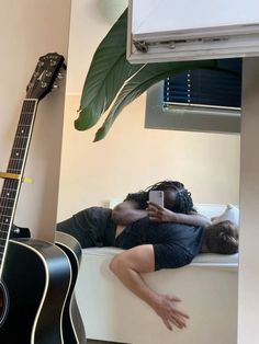 a man laying on top of a bed next to a guitar and a window sill