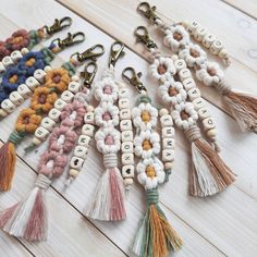 several tasseled key chains with letters and flowers are laid out on a wooden surface