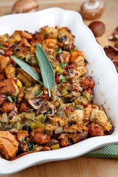 a casserole dish filled with stuffing and vegetables on a wooden table next to mushrooms