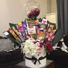 a bouquet of flowers and candy sits on a table in front of a black couch