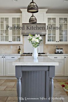 an island in the middle of a kitchen with white cabinets and flowers on top of it